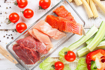 Products for a diet - raw meat of beef and chicken, a salmon and vegetables on a light wooden background. Selective focus.