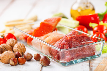 Products for a diet - raw meat of beef and chicken, a salmon and vegetables on a light wooden background. Selective focus.