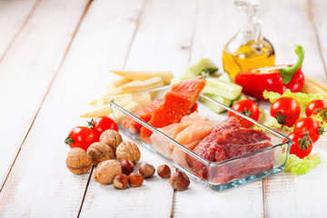 Products for a diet - raw meat of beef and chicken, a salmon and vegetables on a light wooden background. Selective focus.