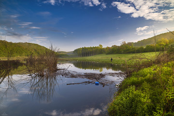 Small lake in the plateau. In the morning in spring. Dry trees in the water. Clouds reflected in calm water.