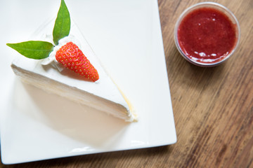 Strawberry crape cake in white plate at top view on wooden.