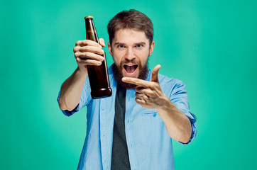 A young guy with a beard on a green background holds a bottle of beer