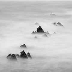 Plakaty  Beautiful long exposure landscape image of sea over rocks during sunset in black and white