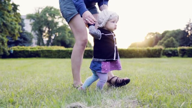 Baby is making first steps on the field in the park against the sunset, slow motion