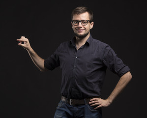 Naklejka premium Young glad man portrait of a confident businessman showing by hands on a black background. Ideal for banners, registration forms, presentation, landings, presenting concept.