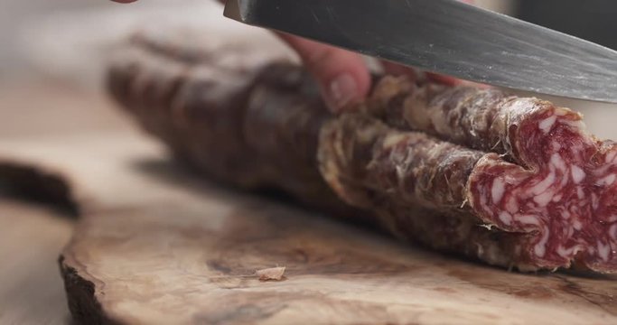 slow motion slide of female teen hand slicing dried italian salami