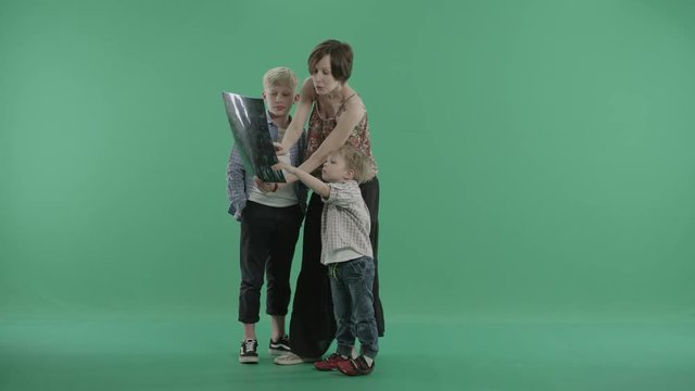 Beautiful pregnant mother stands with her two sons showing them ultrasound scans of a baby