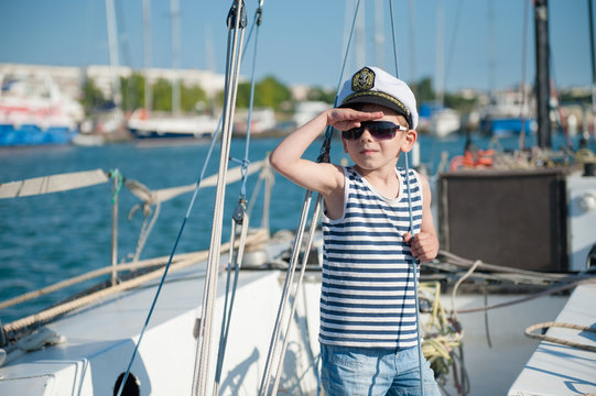 cute little boy captain wearing captain cap and sunglasses aboard luxury boat