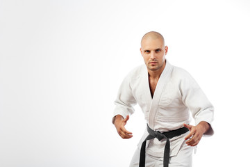 Young man fighter in white kimono with black belt for judo, jujitsu posing in combat pose on isolated white background