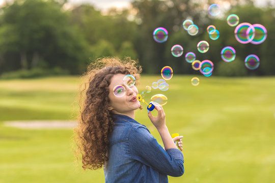 The attractive woman blowing bubbles in the park - Powered by Adobe
