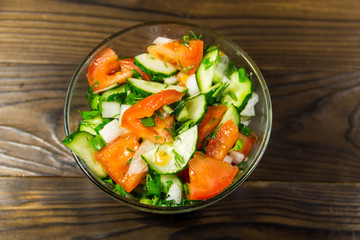 Fresh salad with tomato, cucumber, onion, parsley and dill in glass bowl on wooden table