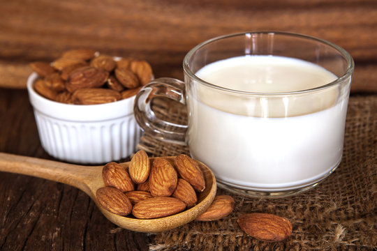 Close up the healthy almond milk in drinking glass with seed in white cup and wooden spoon on wooden table plate
