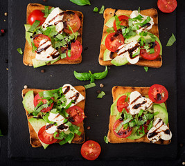 Sandwich toasts with tomatoes, mozzarella, avocado and basil with balsamic vinegar. Flat lay. Top view