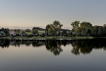 Small houses on the shore of the Lipno dam reflecting in the water at sunset around the woods