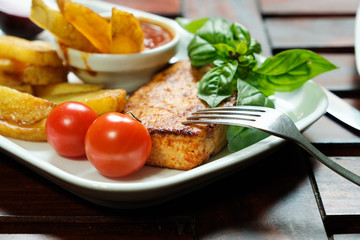 Vegetarian dinner. Fried tofu with spices, potatoes with fresh tomatoes. On a white plate, wooden background.