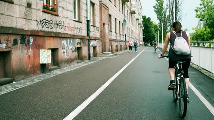 Fototapeta na wymiar Unknown young woman with backsack riding her bicycle along urban bike path