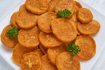 Baked sweet potatoes in white plate on a white wooden table with parsley, garlic and salt. White wooden rustic picnic table scenery from above.