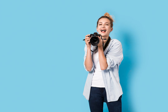 Young blonde photographer is enjoying her work. Model isolated on a blue background with copy space