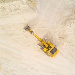 Aerial view of excavator working in quarry or construction site. Industrial top view background concept.