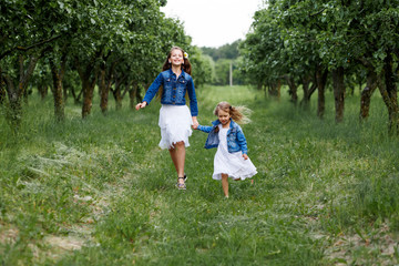 Naklejka na ściany i meble Two sisters having fun outside in summer running in the apple tree garden