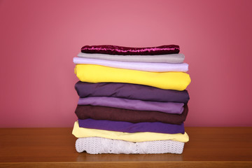 Stack of clothes on wooden table. Combination of lilac and yellow colors