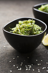 Salad Chukka from seaweed healthy food in dark ceramic bowls on a dark background with lemon slices and light sesame. Top view. Selective focus