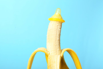 Condom on banana against color background. Safe sex concept - obrazy, fototapety, plakaty