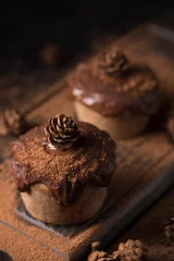  Chocolate muffins, decorated with a small cone on a dark wooden background. Low key. Cupcakes are poured with dark chocolate and cocoa powder. Cupcakes with unusual decoration. © danilsneg