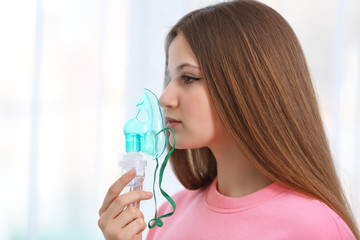 Young woman using nebulizer for asthma and respiratory diseases on light background