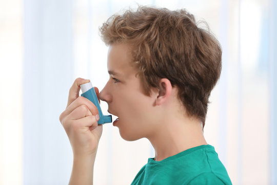 Young boy using inhaler for asthma and respiratory diseases on light background