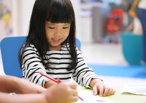Asian children cute or kid girl smile and learning for coloring or paint on white paper with teacher or mother at nursery or school on soft focus
