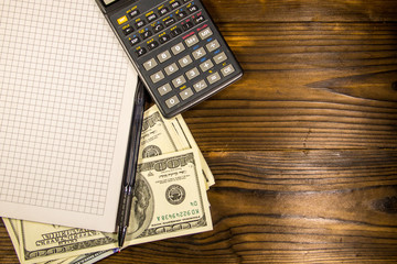 Notebook with dollars, pen and calculator on wooden desk