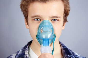 Young boy using nebulizer for asthma and respiratory diseases on light background