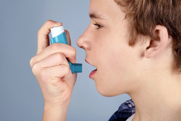 Young boy using inhaler for asthma and respiratory diseases on light background - obrazy, fototapety, plakaty
