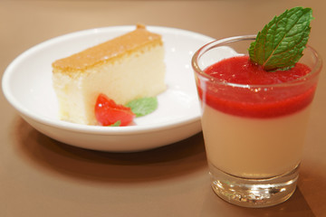 delicious raspberry panna cotta in clear glass and cherry cheese or butter cake on wood table and warm white for sweet dessert or snack at cafe restaurant for breakfast or dinner and background