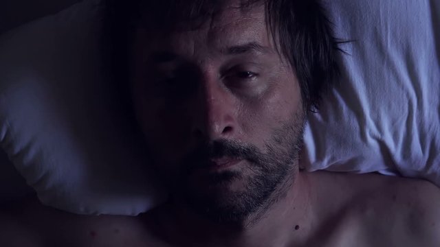 Morning depression and midlife crisis of a man in his 40s lying in bed in morning with symptoms like extreme sadness, frustration, anger and fatigue.
