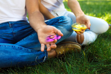 Young girl and boy playing with a fidget spinners in the park. stress relieving toy. Sunny summer day. They laugh and smile. Great mood.
