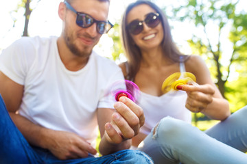 Fototapeta premium Young girl and boy playing with a fidget spinners in the park. stress relieving toy. Sunny summer day. They laugh and smile. Great mood. 