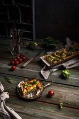 Slice of delicious homemade quiche with cherry tomatoes and broccoli on metal plate. Dark photo of healthy vegetarian food.