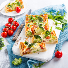 Delicious vegetarian homemade pie, sliced quiche with cherry tomatoes, broccoli and herbal cheese on old white cutting board. Healthy food concept.