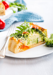 Slice of delicious vegetarian homemade quiche with cherry tomatoes and broccoli on white plate. Healthy food concept.