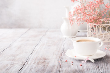 White cup of coffee with pink flowers on old white wooden background with copy space.