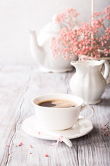 White cup of coffee with pink flowers on old white wooden background with copy space.