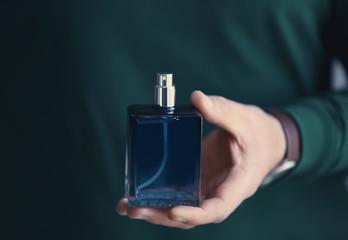 Young man with bottle of perfume, closeup