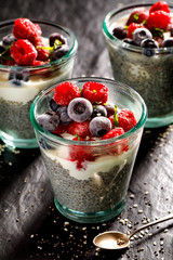 Chia pudding with addition of  raspberries and blueberries in the glasses on a black background, healthy diet concept