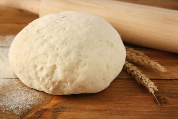 Ball of raw dough, wheat and rolling pin on wooden background