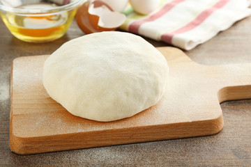 Cutting board with ball of raw dough on wooden table