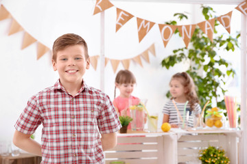 Obraz premium Cute little boy and blurred stand with lemonade on background