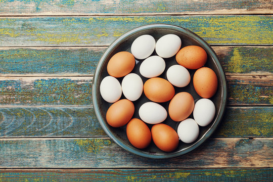 White And Brown Chicken Eggs In Vintage Bowl On Rustic Wooden Table From Above. Organic And Farm Food.