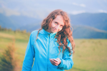 Curly girl texting on smartphone in the mountains during sunset